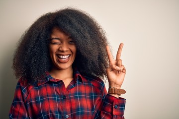 Young beautiful african american woman wearing casual shirt over isolated background smiling with happy face winking at the camera doing victory sign. Number two.