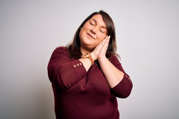 Beautiful brunette plus size woman wearing casual sweater over isolated white background sleeping tired dreaming and posing with hands together while smiling with closed eyes.