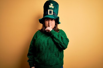 Young beautiful plus size woman wearing green hat with clover celebrating saint patricks day asking to be quiet with finger on lips. Silence and secret concept.