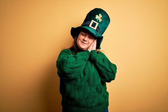 Young beautiful plus size woman wearing green hat with clover celebrating saint patricks day sleeping tired dreaming and posing with hands together while smiling with closed eyes.