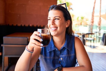 Young beautiful woman sitting at restaurant enjoying summer vacation drinking fresh soda