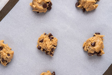 Chocolate Chip Cooke Batter Dollops on a cookie sheet with parchment paper, ready for the oven 