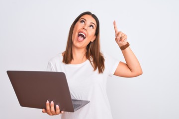 Beautiful young woman working using computer laptop over white background smiling amazed and surprised and pointing up with fingers and raised arms.