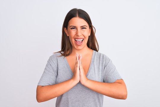Portrait of beautiful young woman standing over isolated white background praying with hands together asking for forgiveness smiling confident.