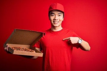 Young handsome chinese delivery man holding deliver box with delicious Italian pizza with surprise face pointing finger to himself