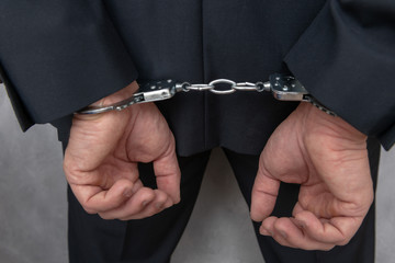 Arrested businessman or official in handcuffs with hands behind back. Corruption or economic crime...