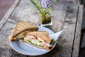 Sandwich with egg, ham, vegetables on plate on table.