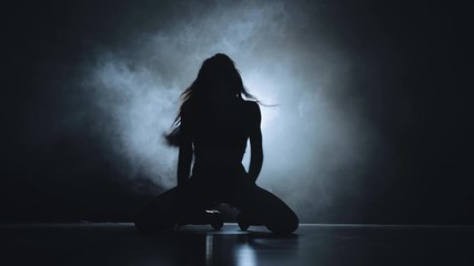 Silhouette of a sexy girl dancing sexy dance in high heels with light in her back. Black smoke background