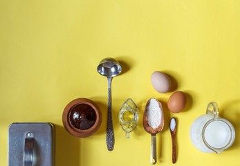 Ingredients and kitchen accessories for making pancakes on a yellow background, top view