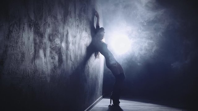Silhouette of a sexy girl dancing sexy dance in high heels with light in her back. Black smoke background