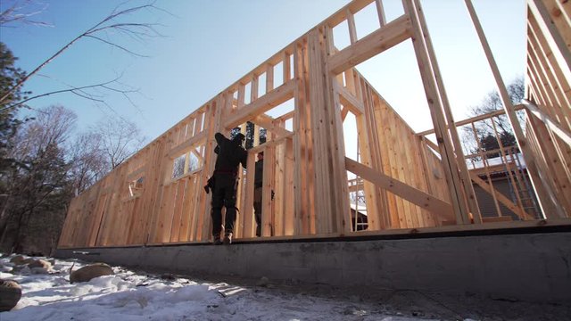 Sliding view from below of framers working at frame residential house building, attaching wooden planks. Sunny winter day