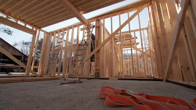 Sliding view of interior of wooden frame of residential house under construction and worker with hydraulic hammer