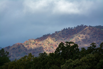 Fototapeta premium Light through the clouds lighting up mountain face lake berryessa california.