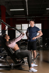 Fototapeta na wymiar Trainer with young woman working out on chest press machine in gym