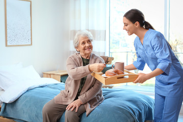 Care worker serving dinner for elderly woman in geriatric hospice
