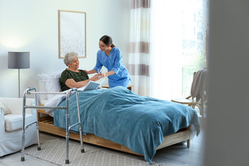 Care worker giving water to elderly woman in geriatric hospice