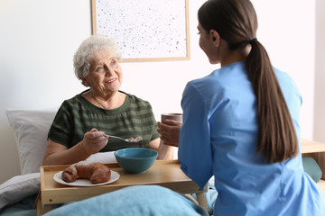 Obraz premium Care worker serving dinner for elderly woman in geriatric hospice