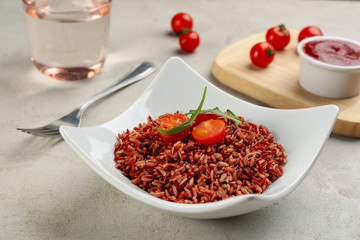 Tasty brown rice with tomatoes on light grey table