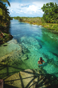 Woman swimming in seven colored lagoon surrounded by tropical plants vertical in Bacalar, Quintana Roo, Mexico