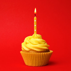 Delicious birthday cupcake with yellow cream and burning candle on red background