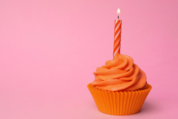 Delicious birthday cupcake with orange cream and burning candle on pink background. Space for text