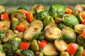Delicious roasted brussels sprouts with bell pepper and peanuts as background, closeup