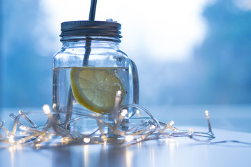 Un verre d'eau et une tranche de citron avec une paille sur une table entourée d'une guirlande lumineuse