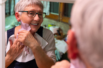 older woman waxing with wax, looking in a mirror