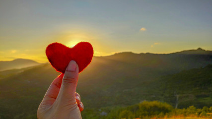 inspirational photo of red heart shape pillow with hand holding it in nature background