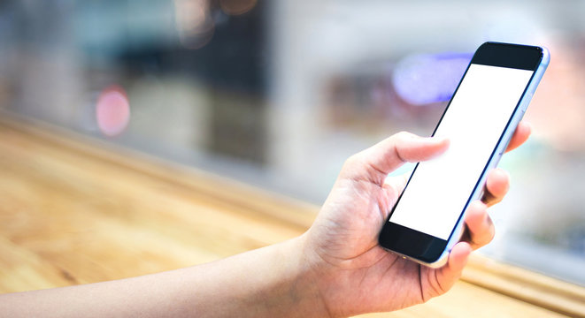 Mockup image of a woman's hand using black mobile phone or smartphone, with the blank white screen and use download application social media in coffee shop. Background blur and bokeh with copy space.