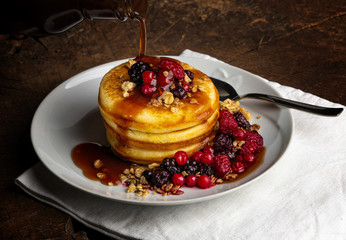 Pancakes with forest fruits berries on wooden table.Blueberries, raspberries on pancakes with maple syrup. Concept morning protein breakfast.