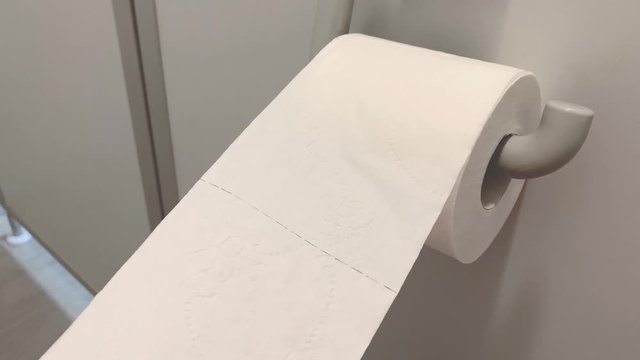 Man's hand pulls toilet paper from a roll in a public toilet