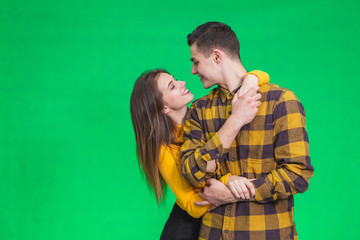 Attractive lovers cuddling, looking one another in eyes, posing on green background.