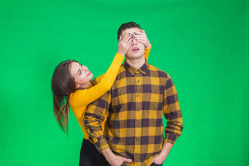 Woman closing his boyfriend eyes to make a surprise for him, he is in anticipation over green background.