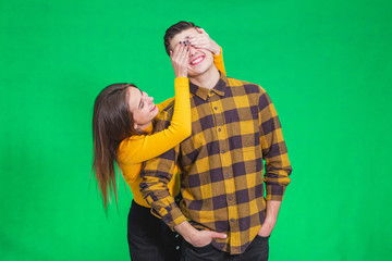 Woman closing his boyfriend eyes to make a surprise for him, he is in anticipation over green background.