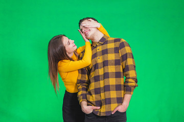 Woman closing his boyfriend eyes to make a surprise for him, he is in anticipation over green background.