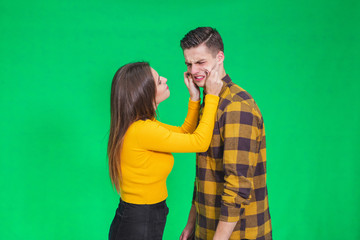 Girl pinching guy's cheeks, making fyn, he is scowling his face, looking completely annoyed.