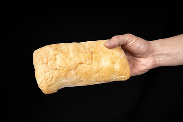 Fresh bread ciabatta in the male hand on black background.