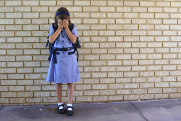 Fototapeta na wymiar Sad young schoolgirl covering her face and crying in school yard