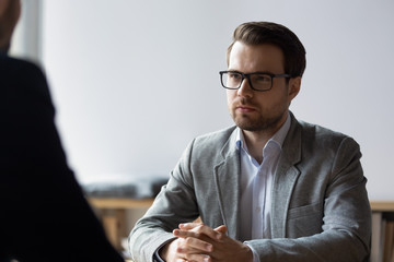 Serious businessman with clasped hands looking at opponent at negotiations