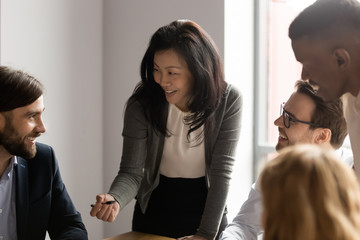 Middle aged Asian businesswoman talking to diverse colleagues at meeting