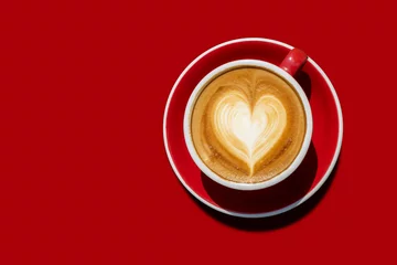 Ansicht von oben Heißer Cappuccino-Kaffee Und mit einer Creme wie dem Herzen in einer roten Tasse auf rotem Grund. isoliert mit Beschneidungspfad. Liebes- und Kaffeekonzept für den Hintergrund © chathuporn