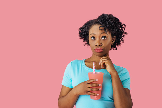 Close Up Portrait Of A Young Woman Holding A Drink With Straw And Looking Up With Raised Eyebrows, Thinking