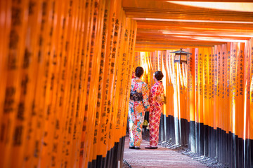 Fototapeta premium women geishas among red wooden Tori Gate at Fushimi Inari Shrine in Kyoto, Japan