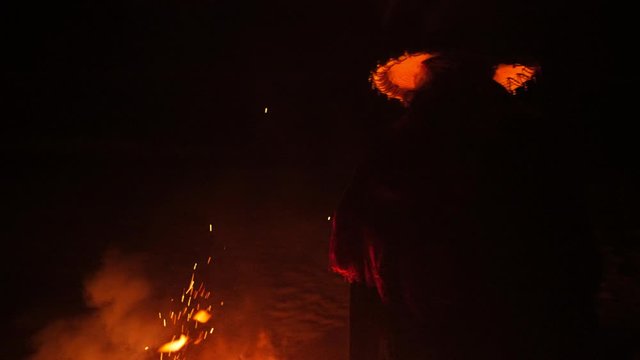 Mysterious shrouded figure dances near bonfire in the twilight