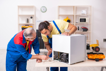 Two contractors repairing fridge at workshop