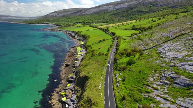Car driving past scenic coastline in West Ireland, forward following aerial