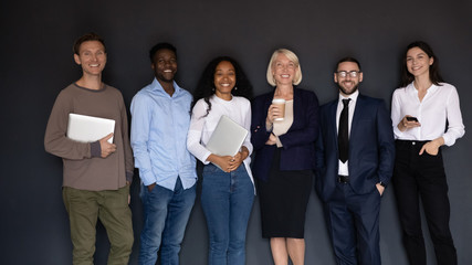 Fototapeta premium Group of multiethnic corporate staff holding gadgets smiling posing indoors