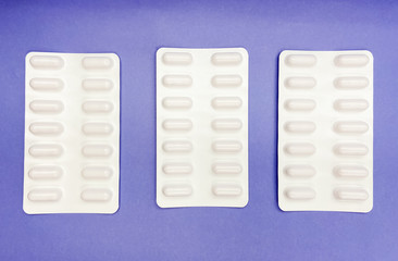 Set of pills in white foil capsule tablet packaging lay flat and isolated on blue background. For pharmaceutical, medical and science theme.