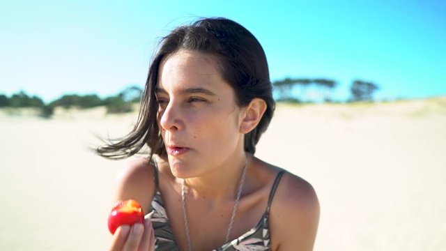 Portrait of young woman eating juicy red plum on the beach, slow motion